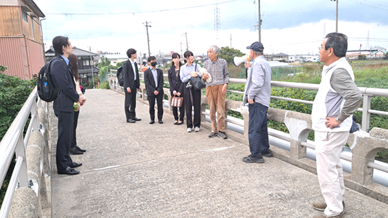 フィールドワーク
男里川にかかる橋の上から「石綿村」と言われた地域（右手後方）について説明する柚岡さん（ハンドマイクを持つ人）